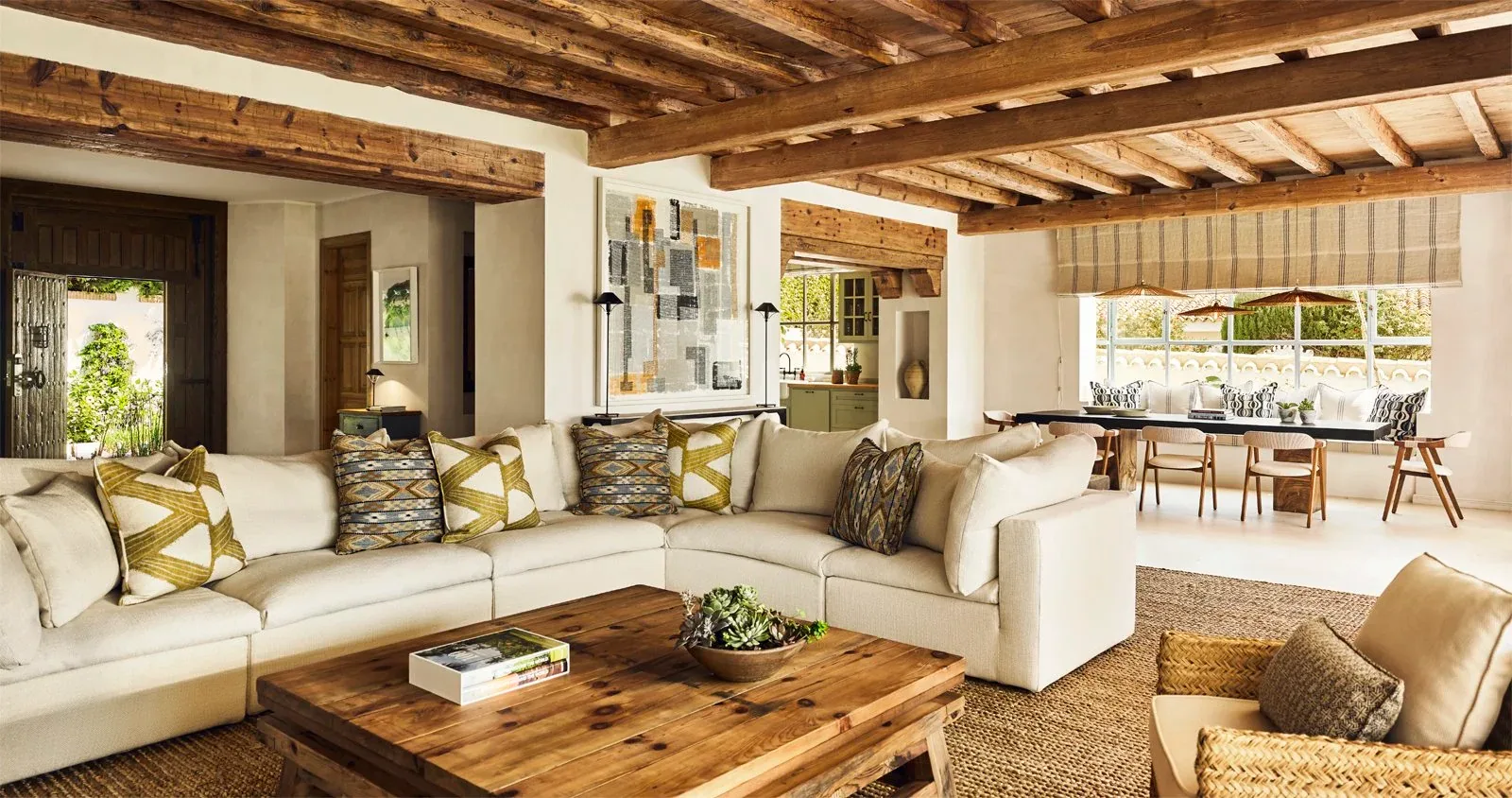 Villa living room with a wooden beamed ceiling, a large cream sofa, a timber coffee table and a dining area