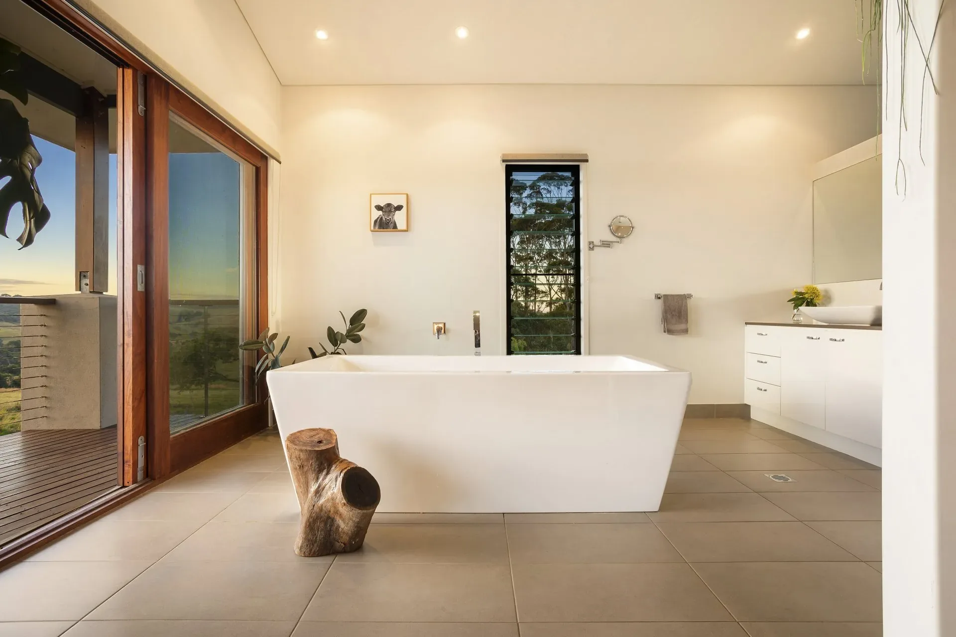 Bathroom with a freestanding white bath, timber stool and tall sliding glass doors