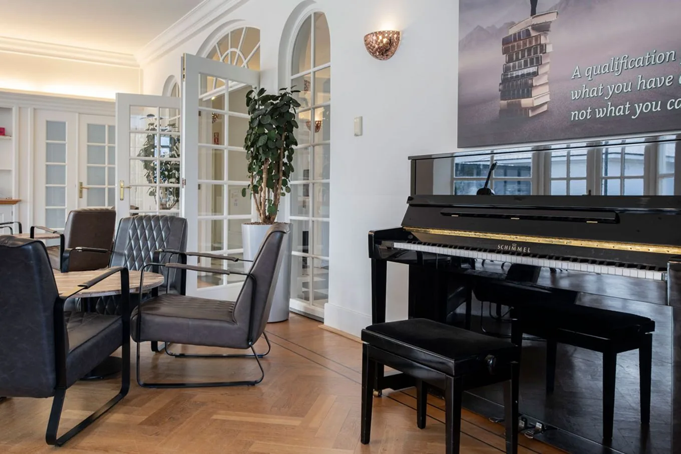 Lounge with an upright piano, grey armchairs, a plant and glazed arched doors along one wall
