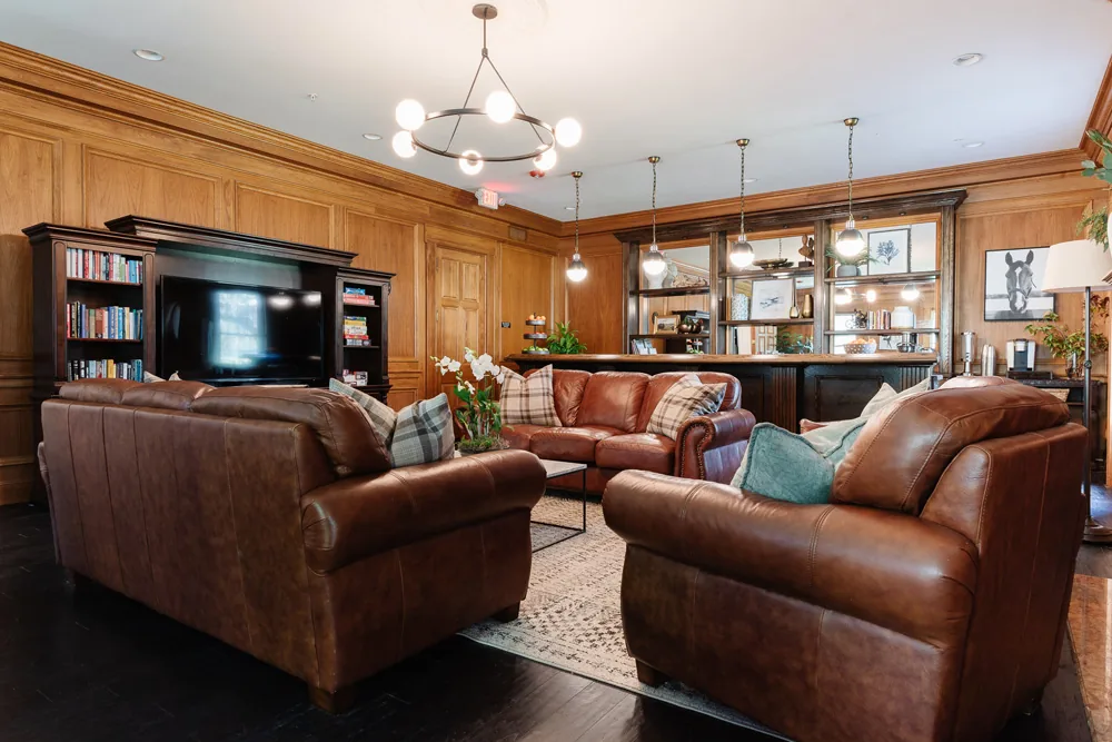 Wood-panelled lounge with brown leather sofas, bookshelves, a television and pendant lights