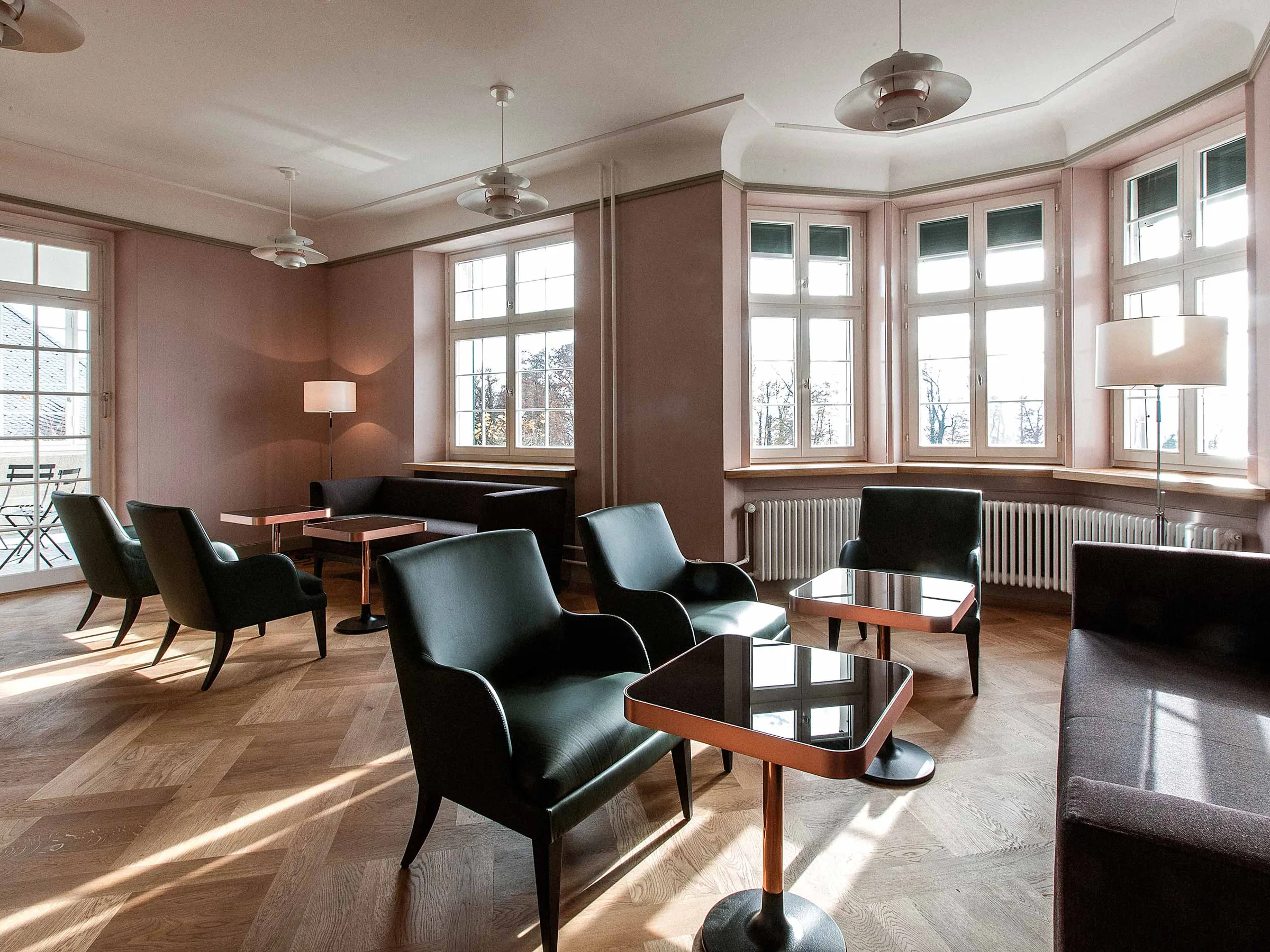 Lounge with black leather armchairs, small tables and bay windows letting in daylight