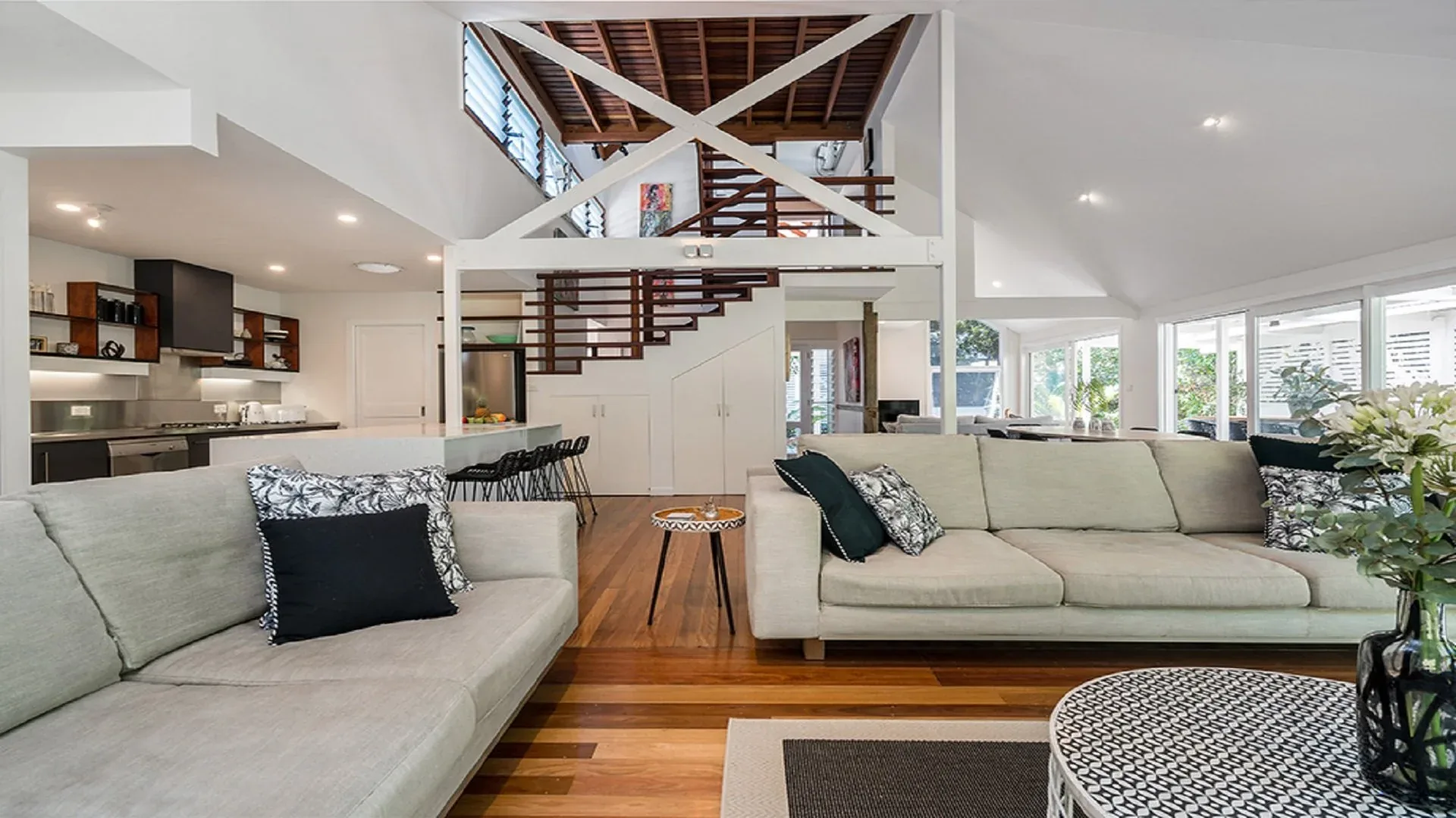 Open-plan living room with cream sofas, timber floors, a high raked ceiling and a staircase