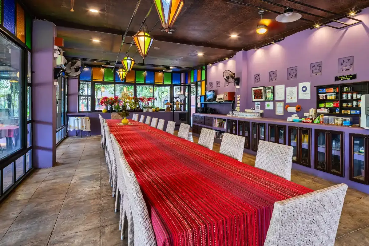 Dining hall with a long table under a red runner, white wicker chairs and hanging star lanterns