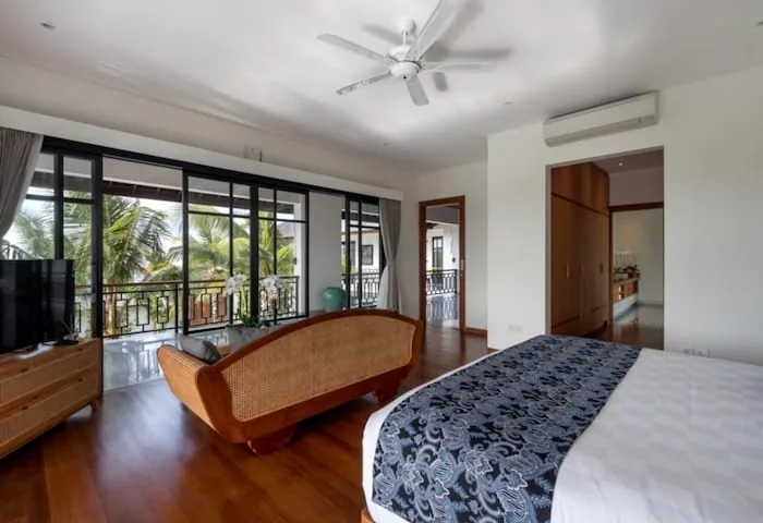 Bright villa bedroom with a wooden floor, a daybed and glass doors to a balcony over palm trees