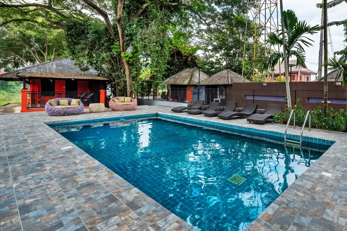 Rectangular outdoor pool with stone paving, sun loungers and shaded salas under tall tropical trees