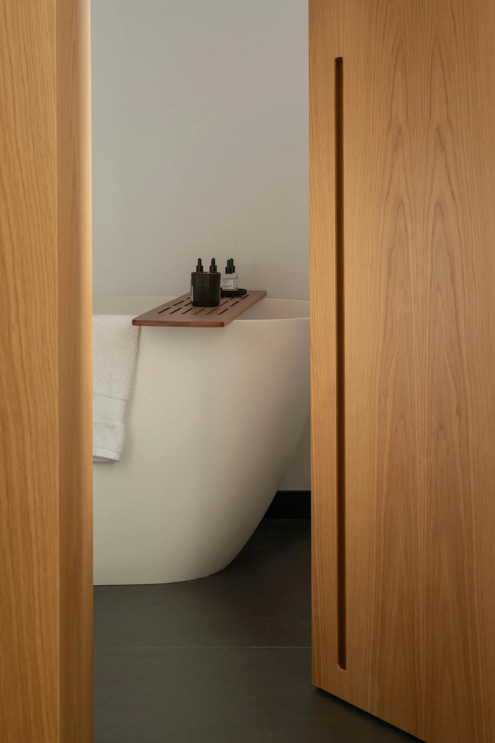 Bathroom with a white freestanding bathtub seen through an open oak sliding door