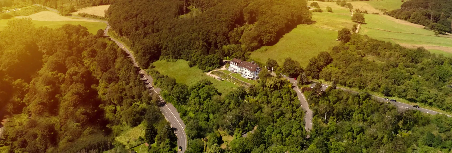 Aerial view of the clinic building among forest and meadows on a hillside in warm evening light