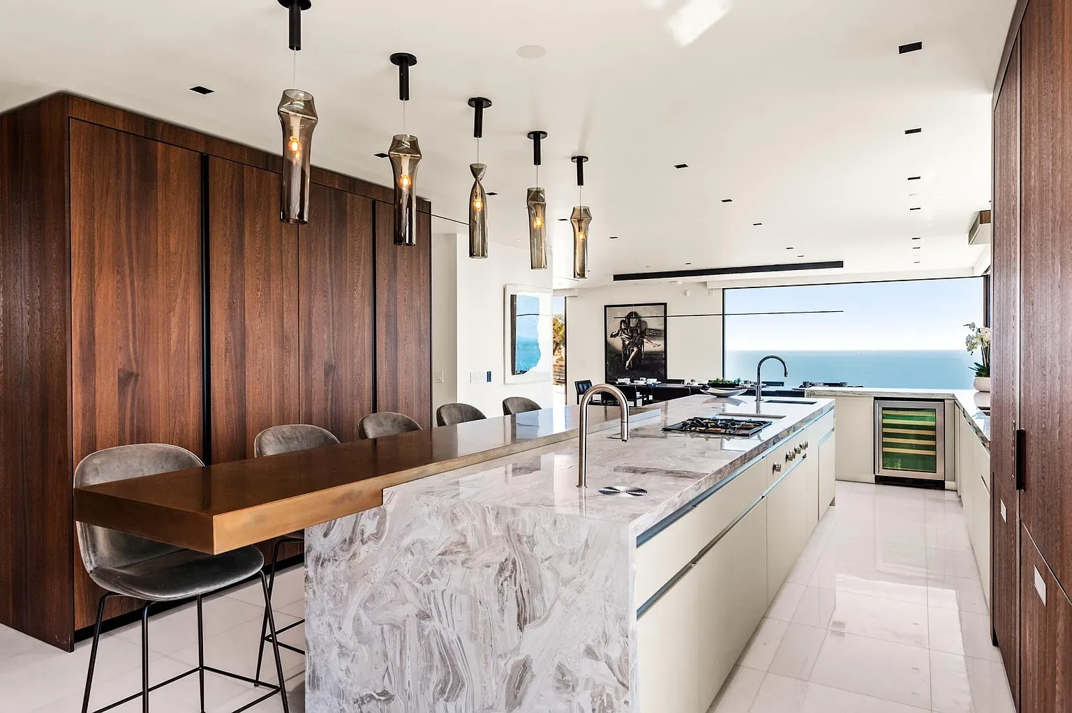 Open kitchen with walnut cabinets, a marble island, bar stools and pendant lights facing the sea