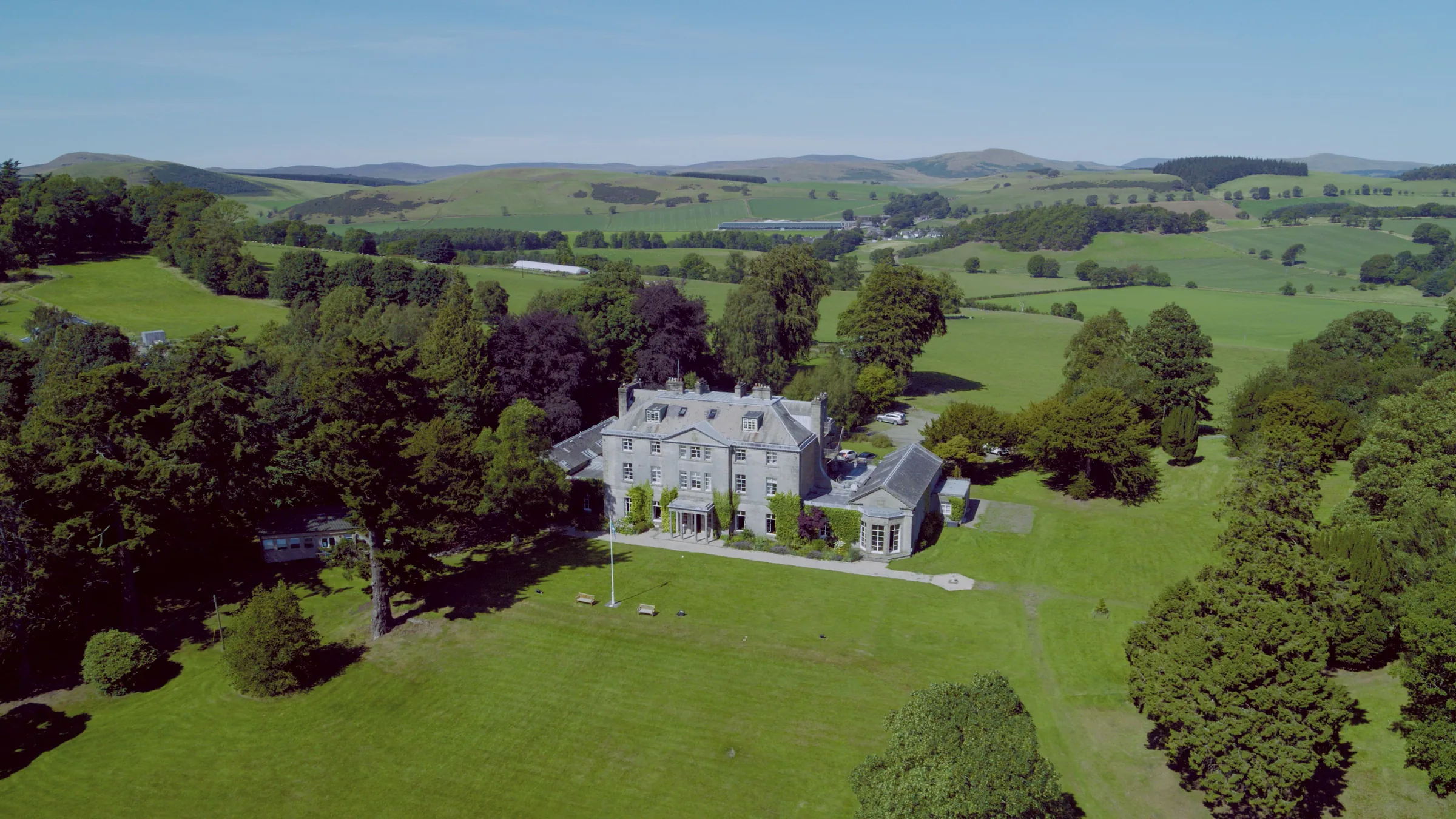 Aerial view of the grey stone country house set in lawns and woodland with rolling hills behind