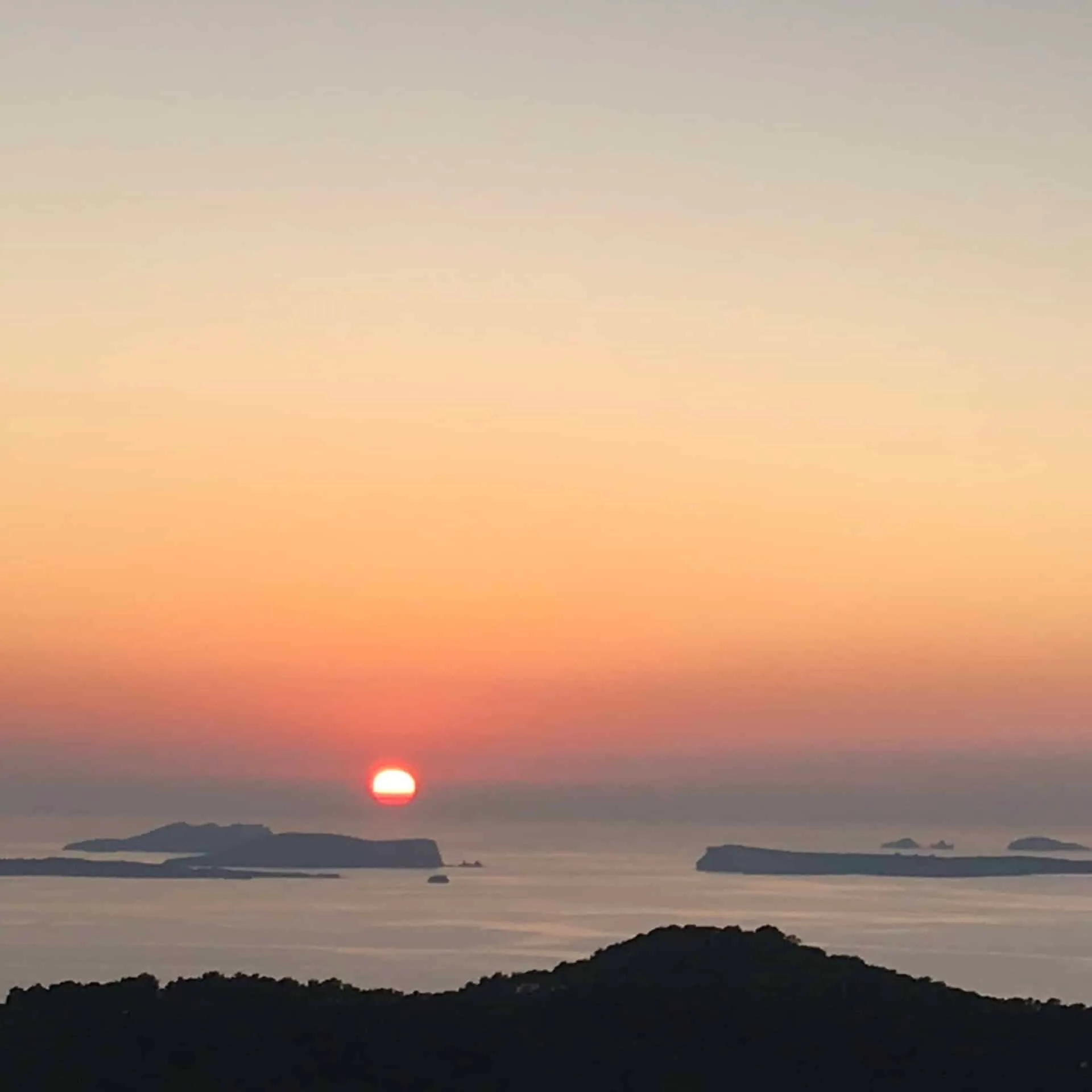 Sun setting over the sea and small islands beyond a dark hillside, seen from an Ibiza residence
