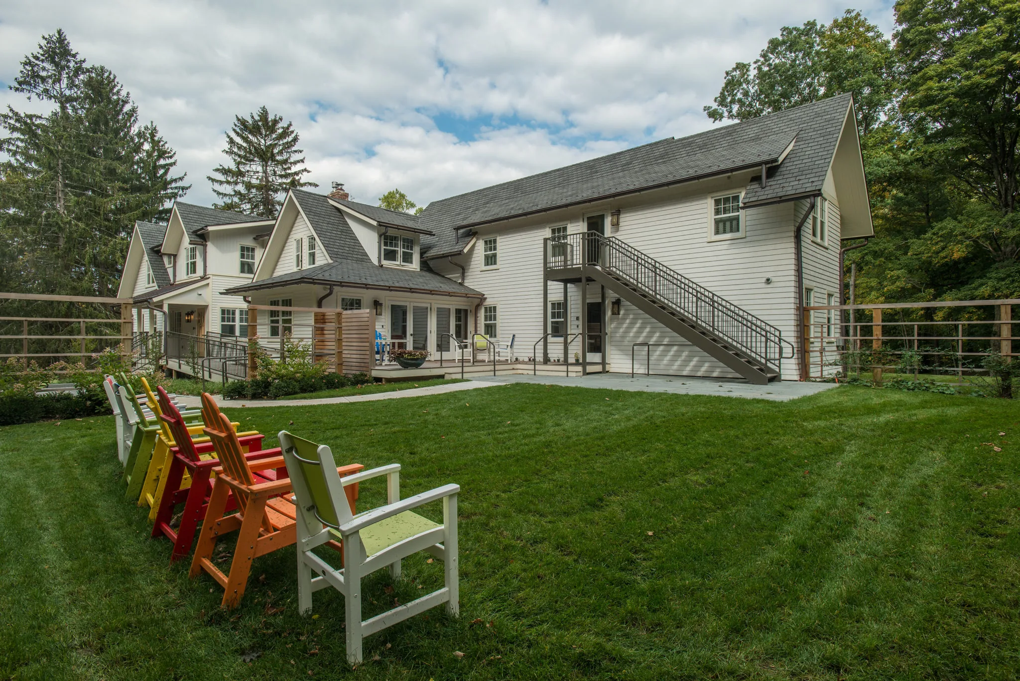 Colourful Adirondack chairs on a mown lawn behind the white clapboard Klingenstein House