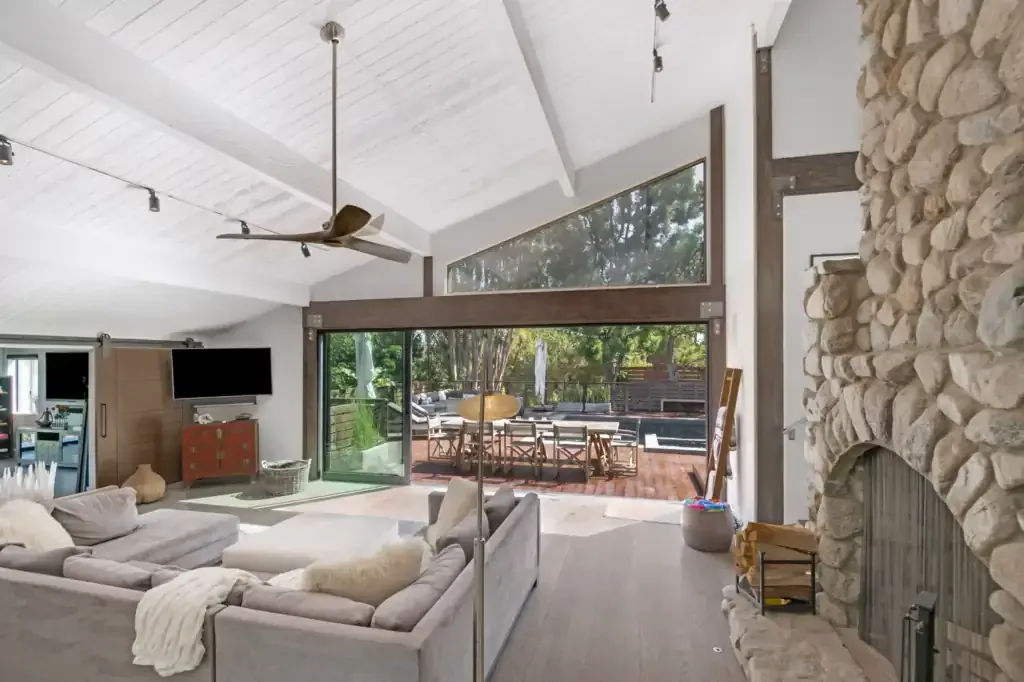 Living room with grey sofas, a river stone fireplace, vaulted white ceiling and doors to a deck