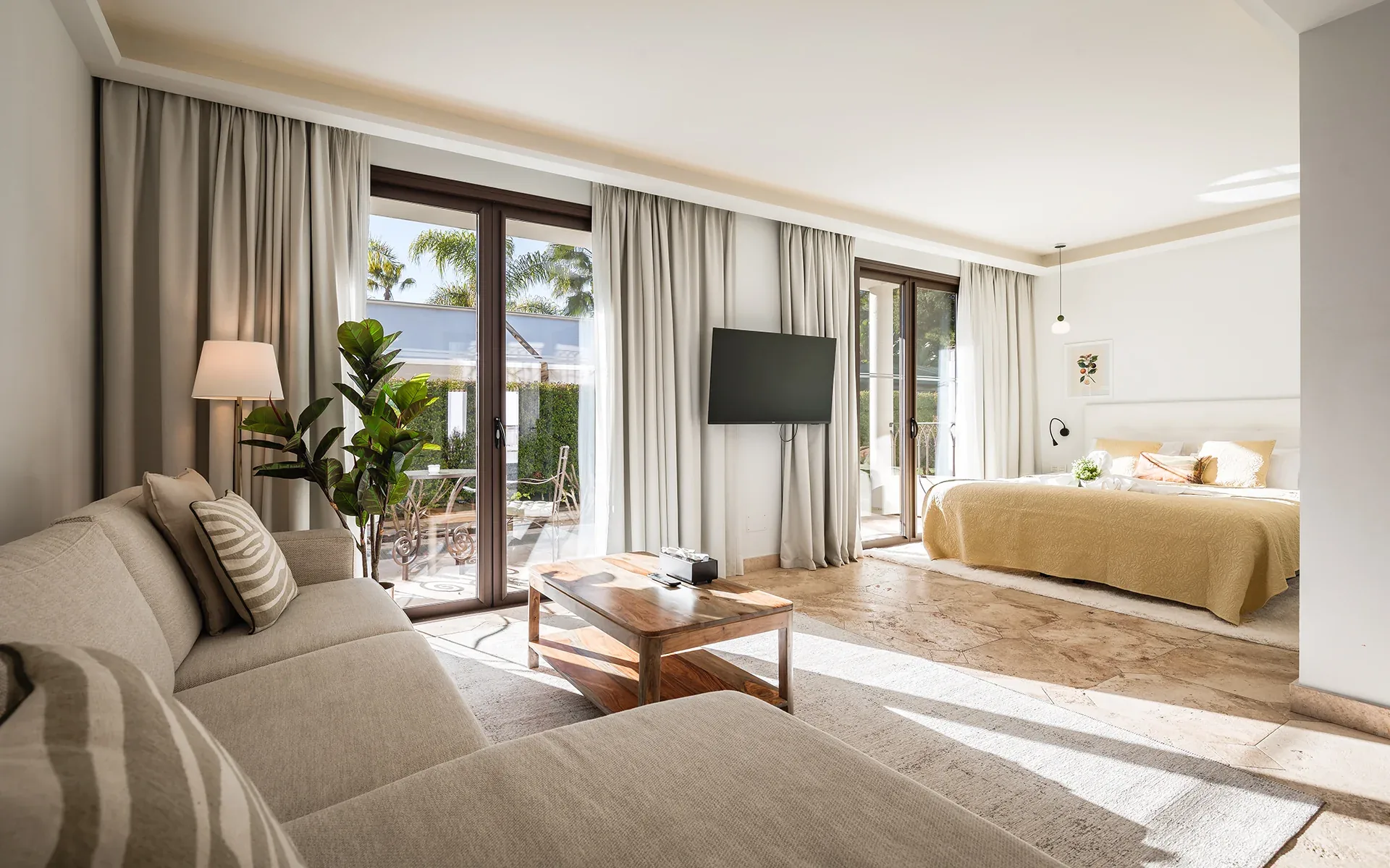 Bright suite with a cream sofa, a double bed, a wall-mounted TV and glass doors to a terrace