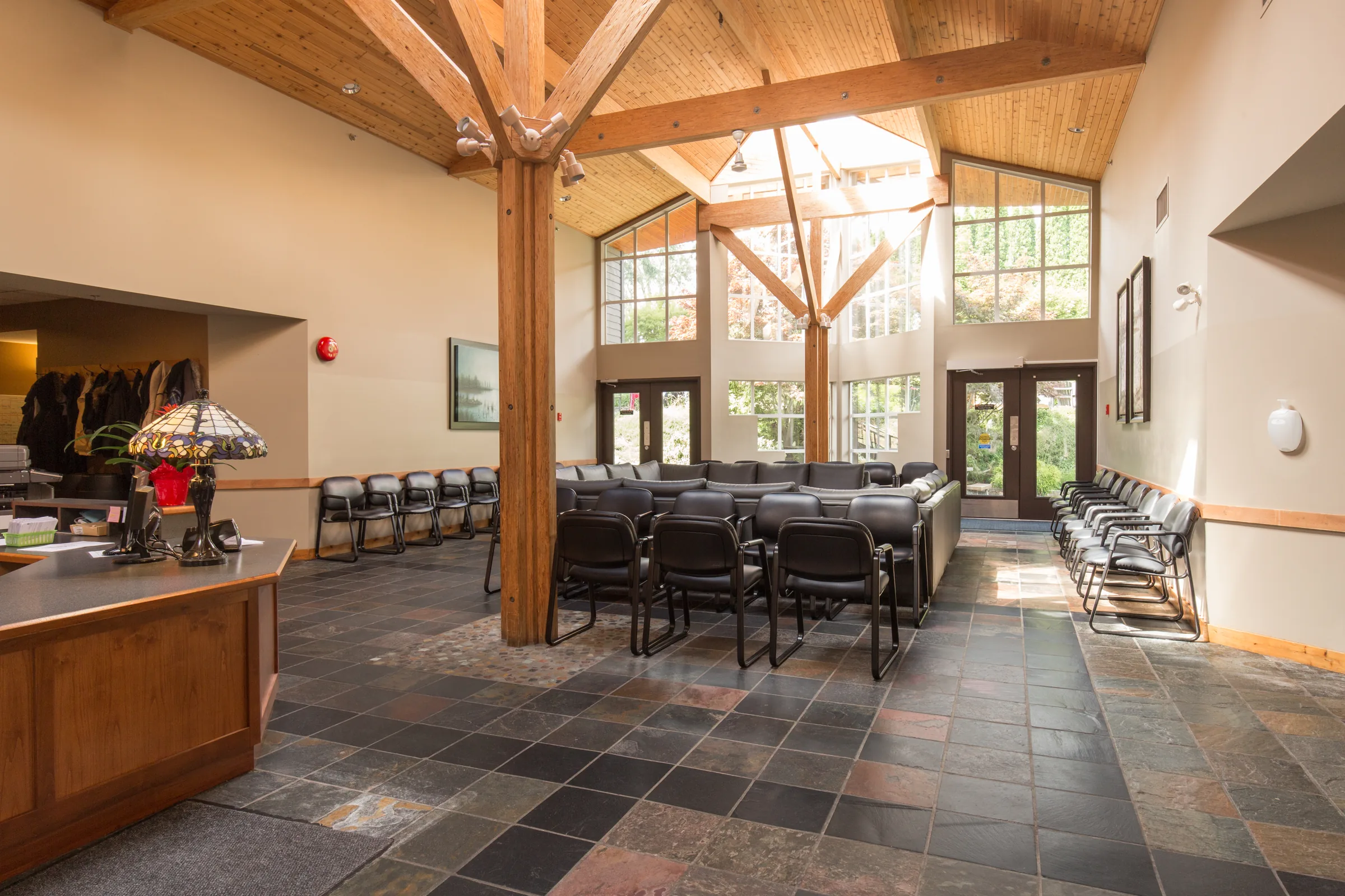 Main lounge with exposed timber trusses, tall windows, slate floor and rows of chairs and tables