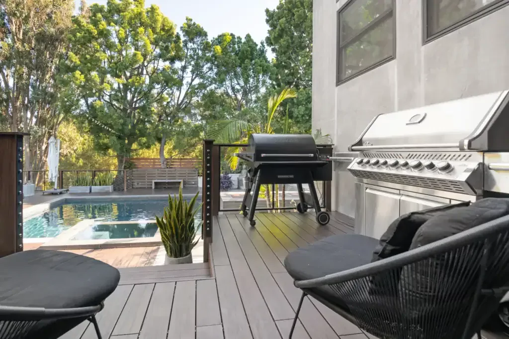 Wooden deck with outdoor chairs and a grill overlooking a swimming pool surrounded by trees