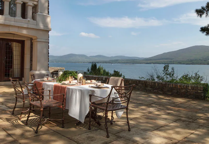 Stone terrace with a laid table and wrought iron chairs overlooking a lake and mountains