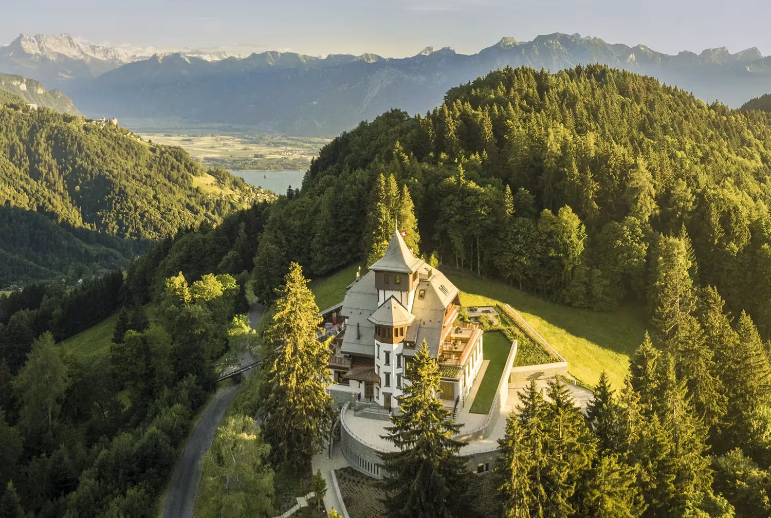 Aerial view of the turreted clinic building surrounded by forest and meadows with a valley below