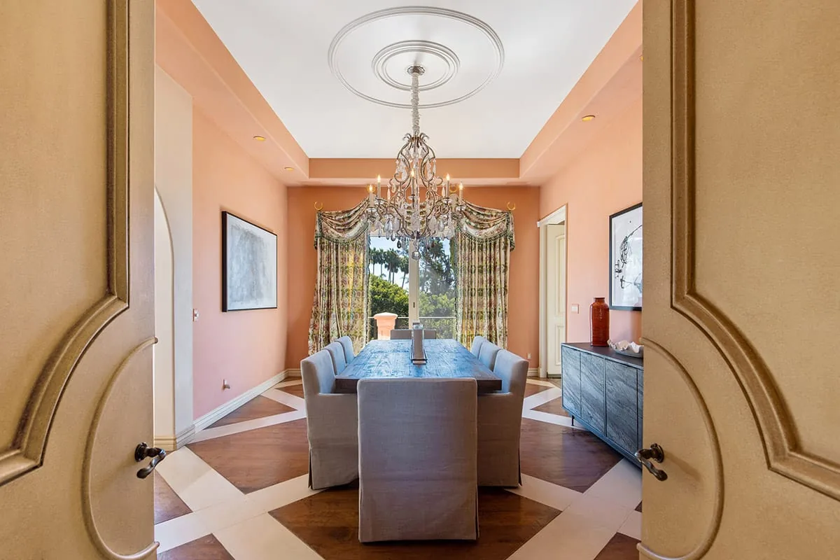 Dining room with peach walls, a crystal chandelier and upholstered chairs around a long table