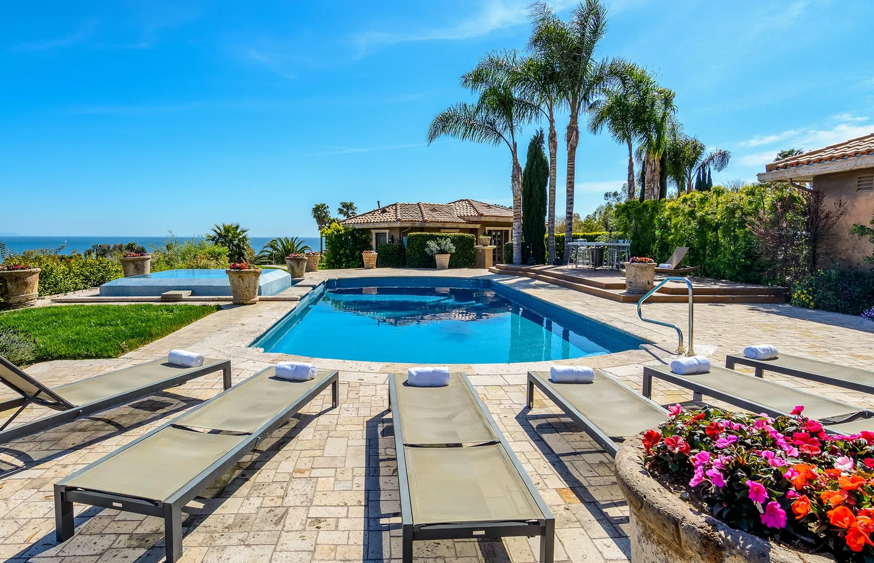 Swimming pool with rows of sun loungers, palm trees and the Pacific Ocean on the horizon
