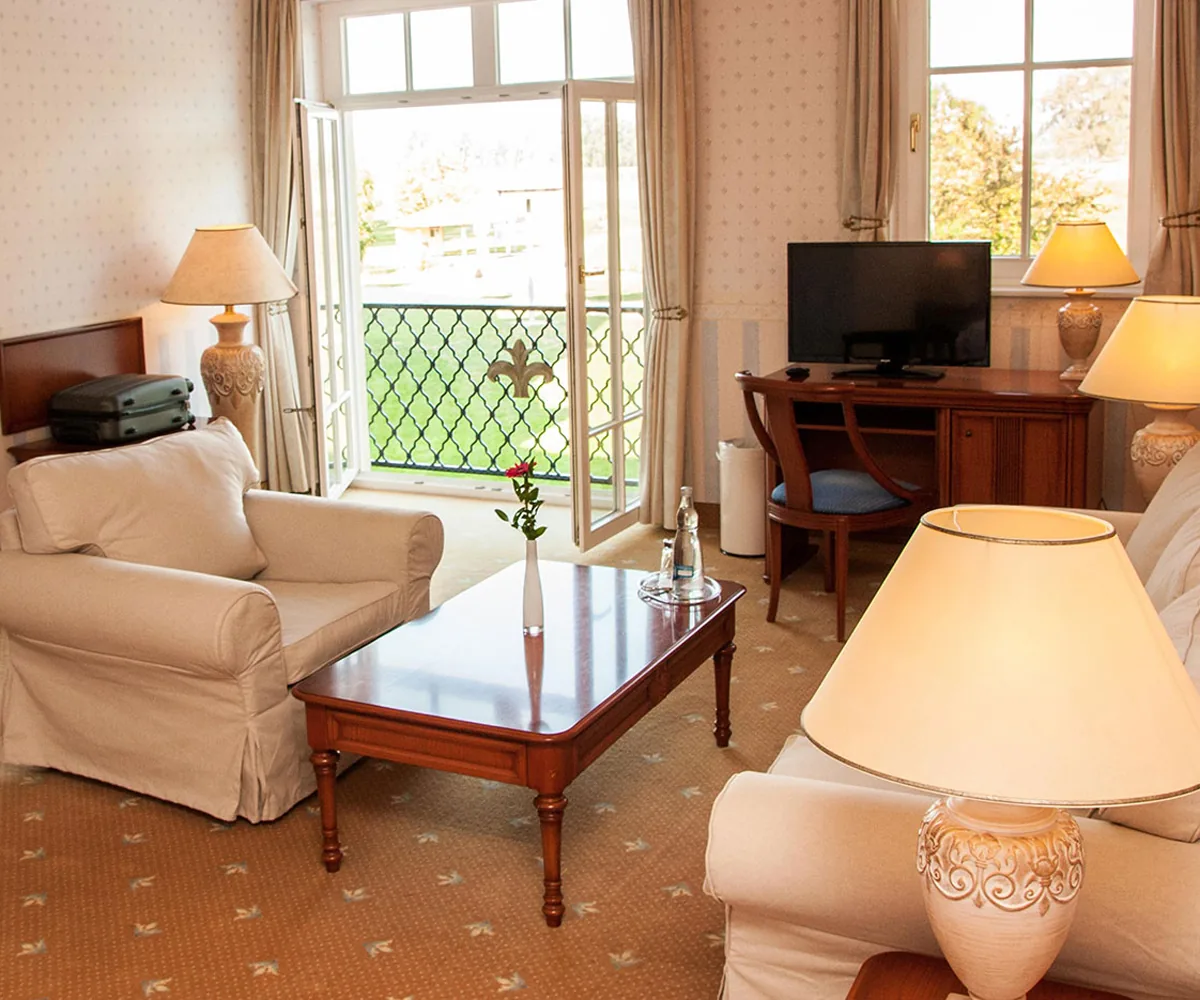 Patient room with armchairs, table lamps, a desk and open French doors to a small balcony