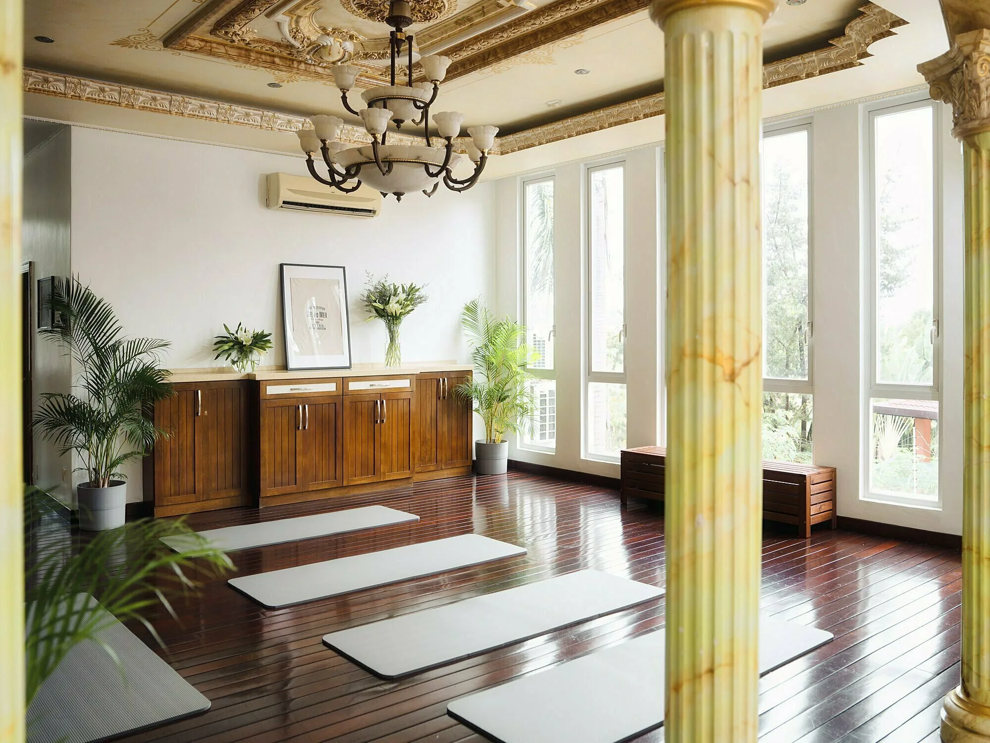 Yoga and dance studio with mats on a wooden floor, marble columns, a chandelier and tall windows