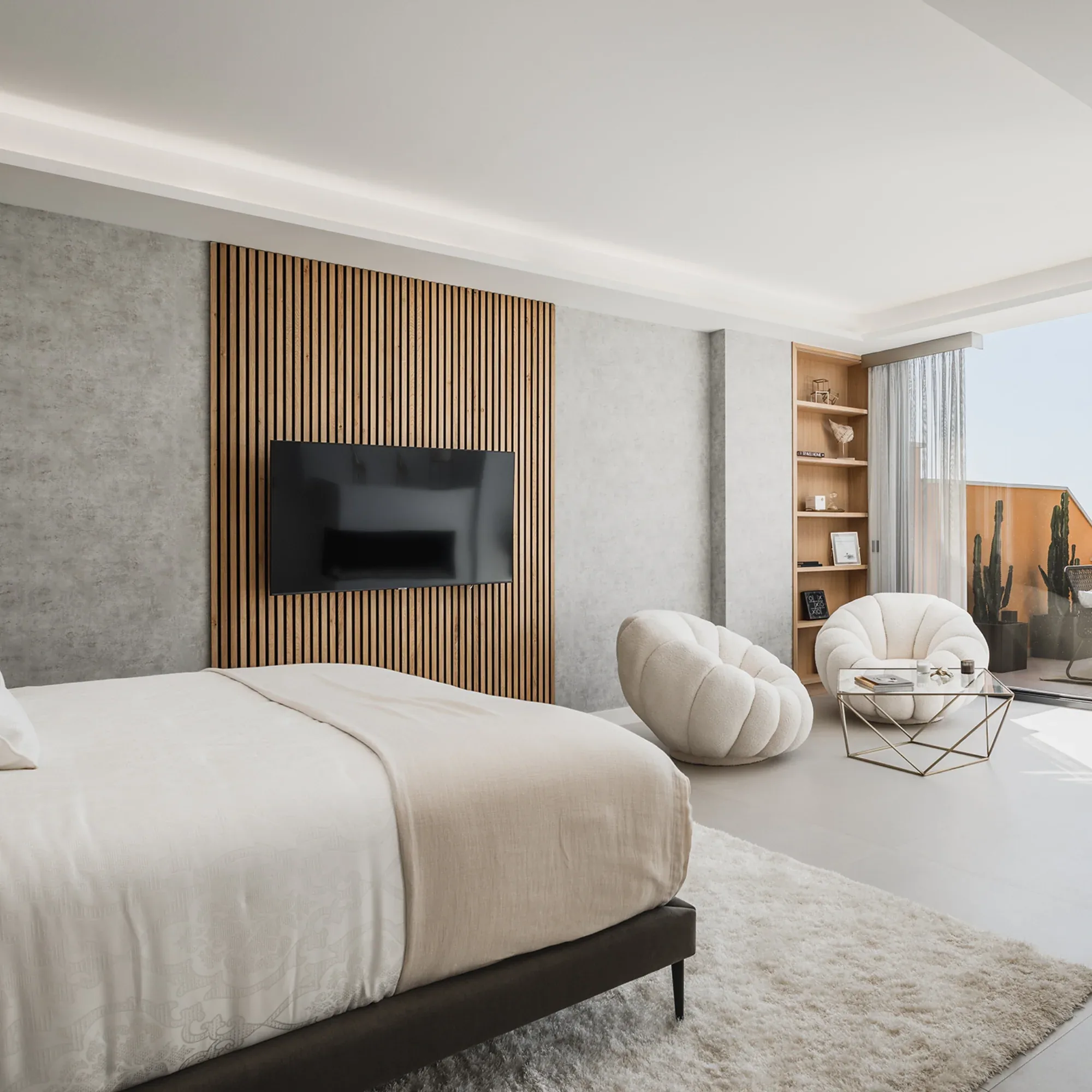 Bright bedroom with a double bed, wood panelled wall with television, armchair and shelving