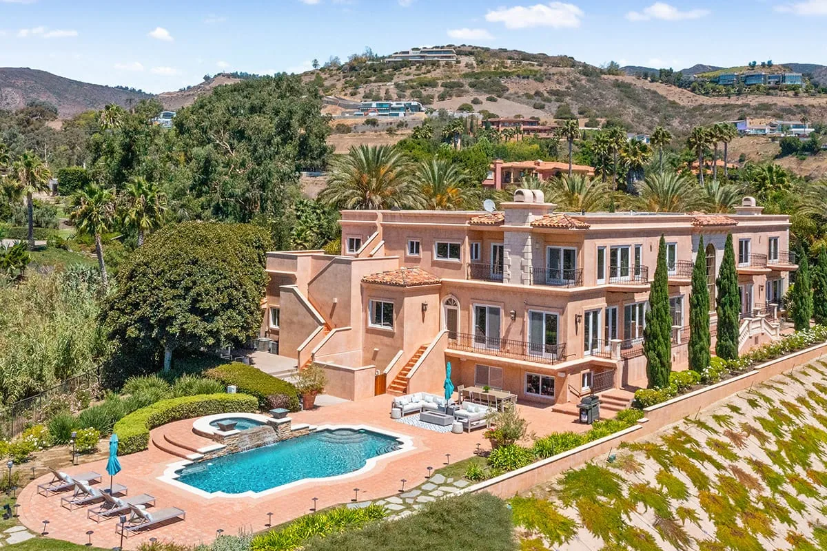 Aerial view of a pink Mediterranean style villa with a pool and terraced gardens on a hillside