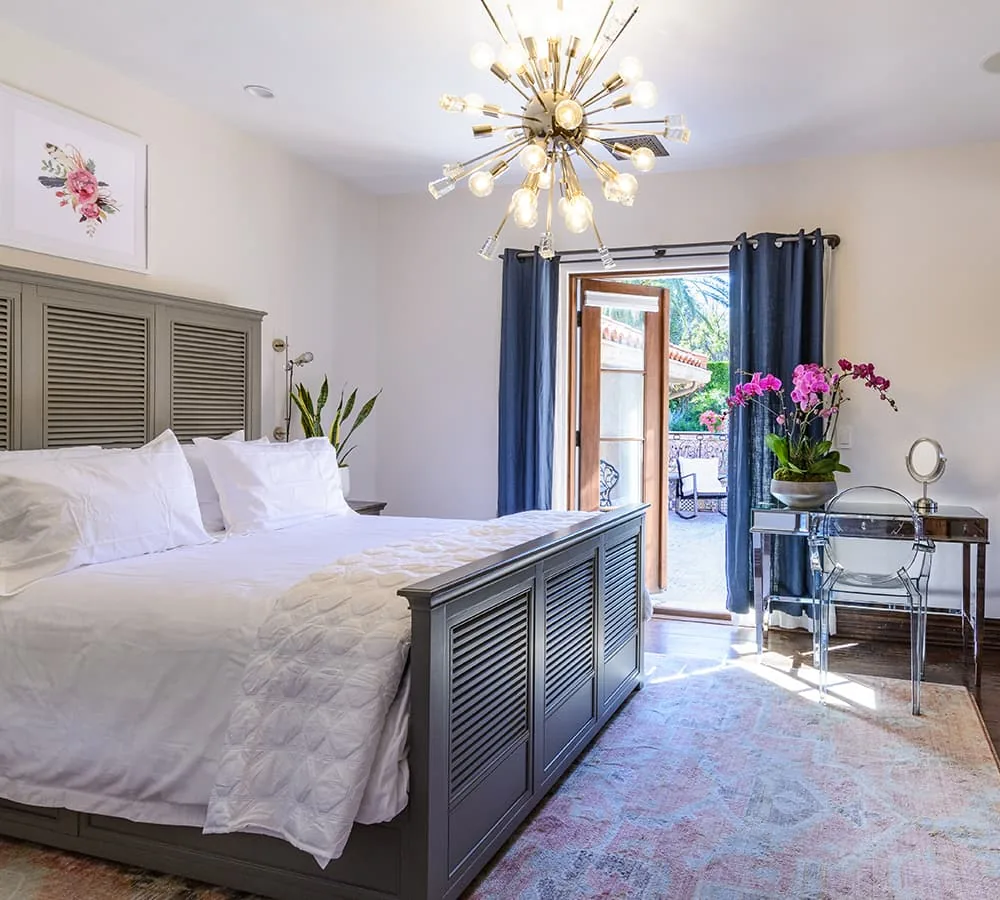 Private bedroom with a tall upholstered headboard, white bedding and open doors to a sunny balcony
