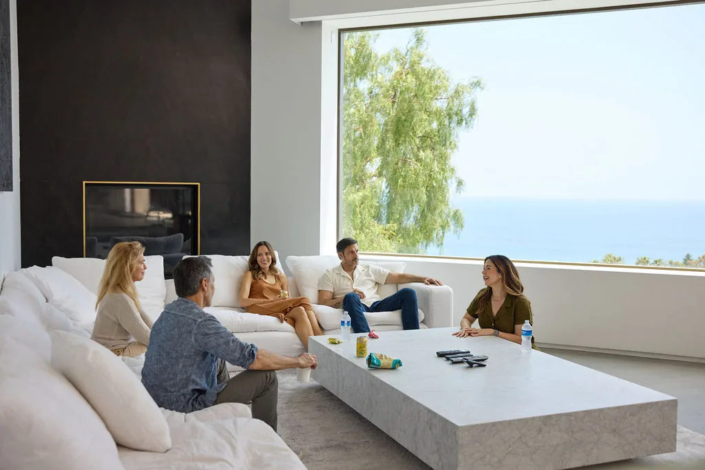 Small group seated on white sofas around a stone coffee table in a living room with ocean views