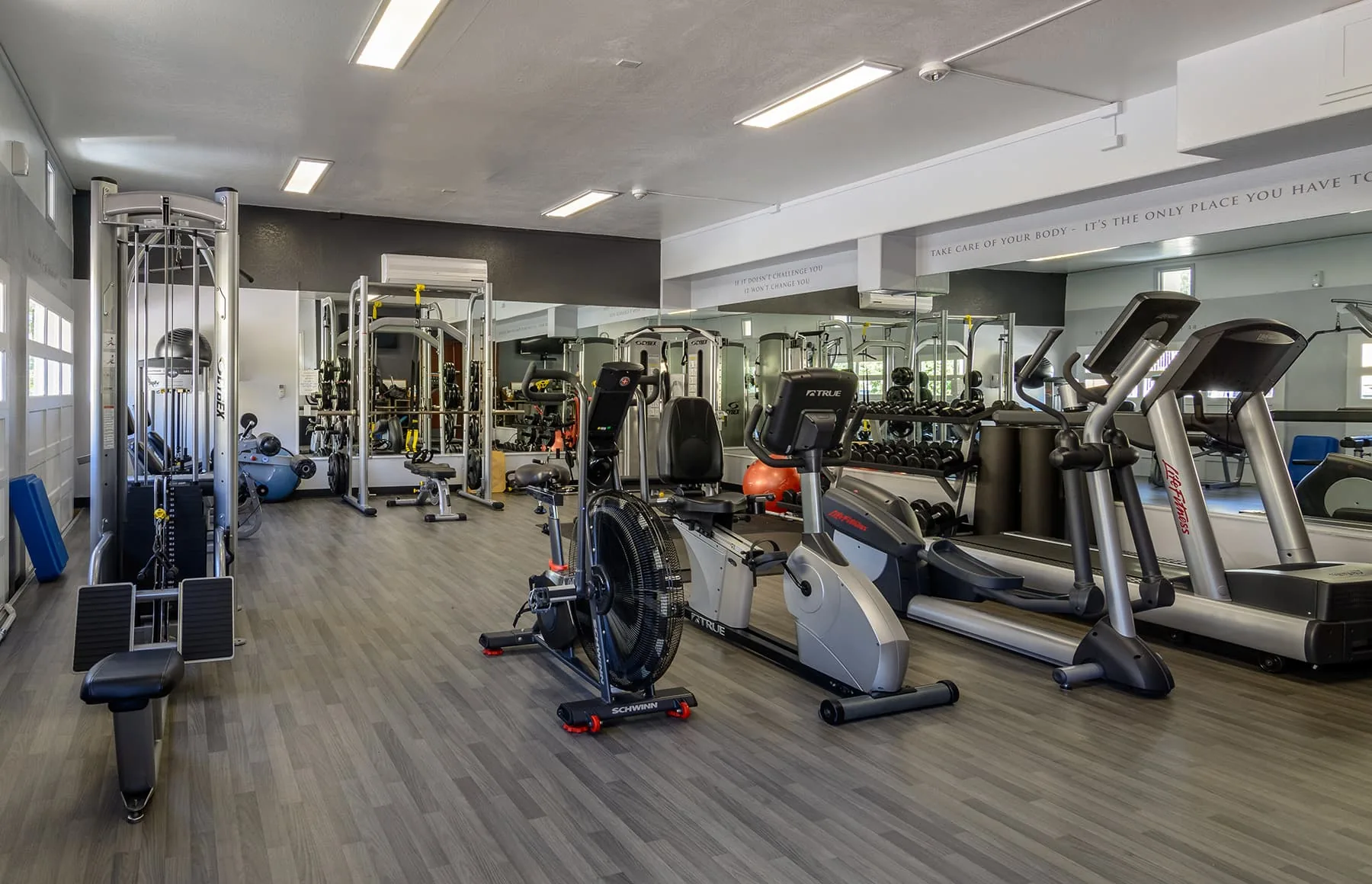 Fitness room with treadmills, an exercise bike and weight machines under bright ceiling lights