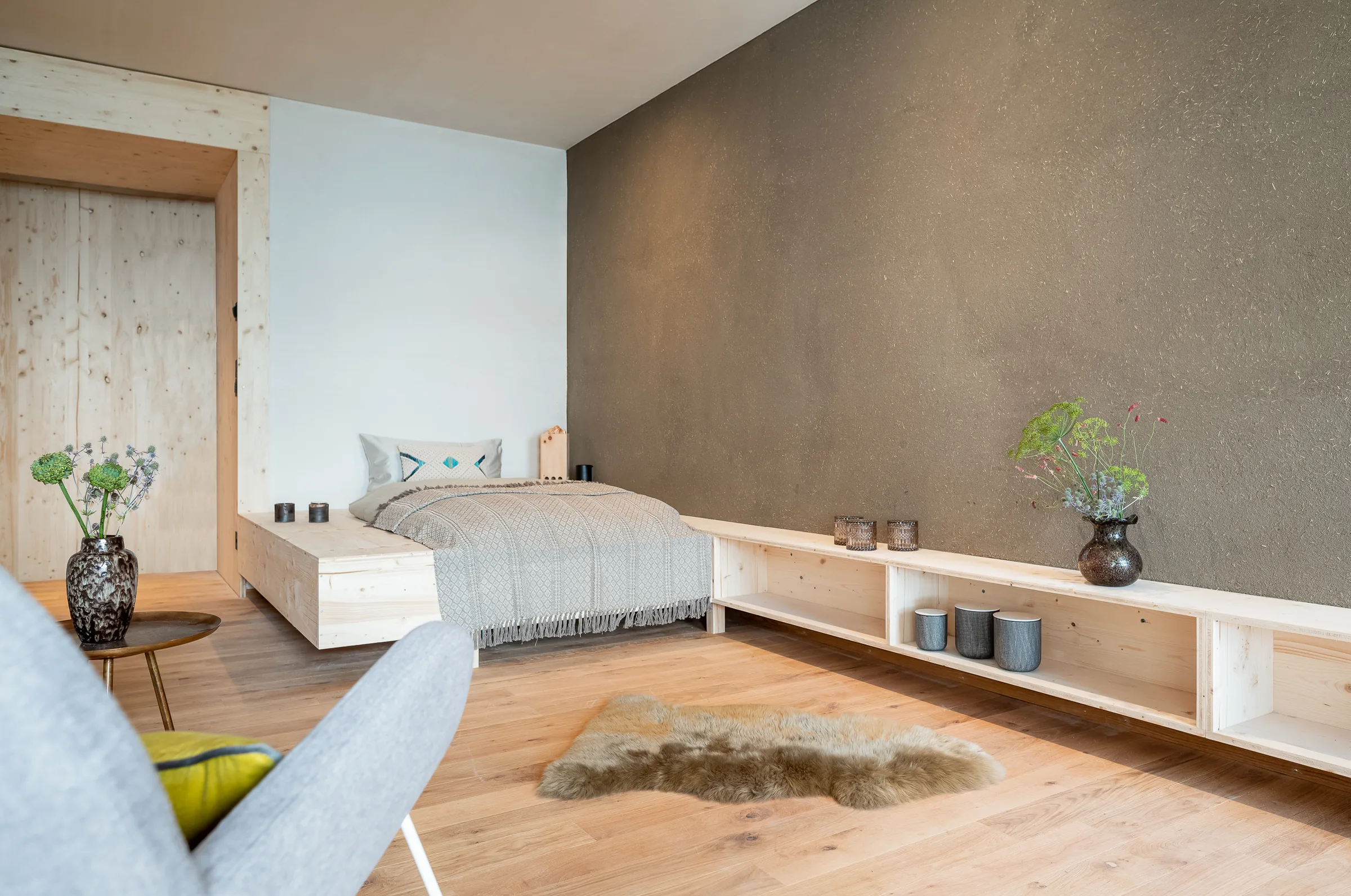 Patient room with a double bed, low built-in timber shelving, light wood floor and a sheepskin rug