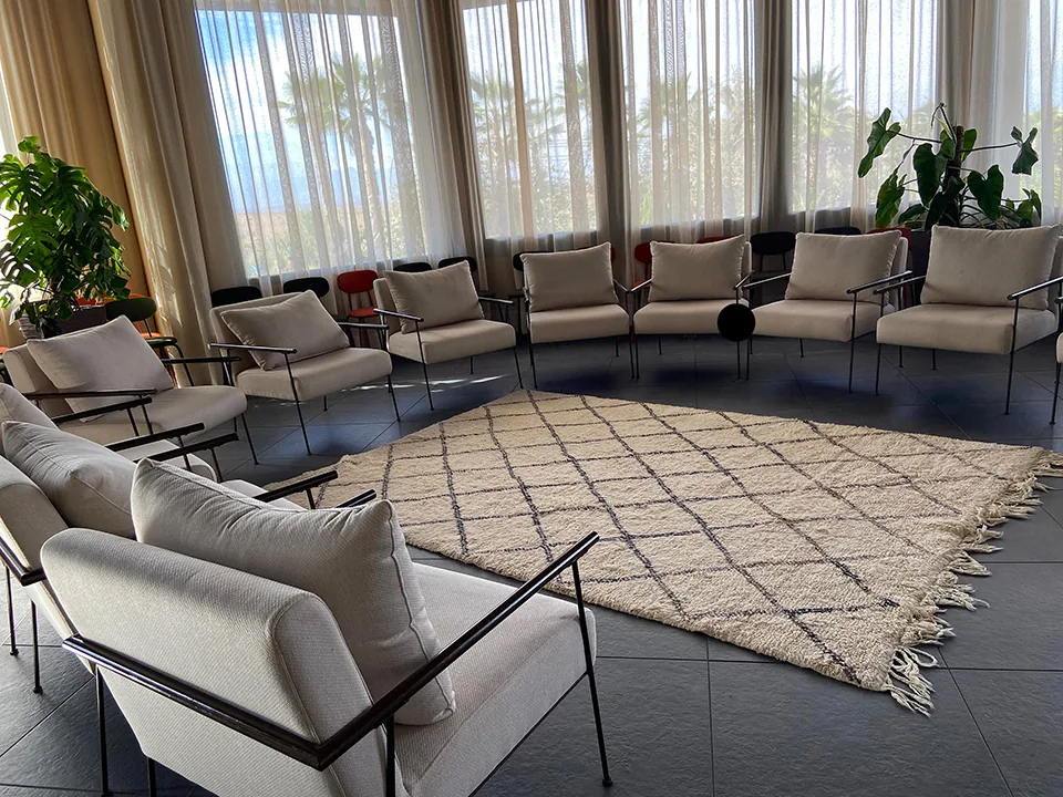 Circle of white upholstered chairs on a Berber rug in a room with tall windows and sheer curtains