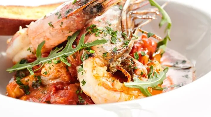 Plated dish of grilled shrimp with tomato sauce and fresh rocket leaves in a white bowl
