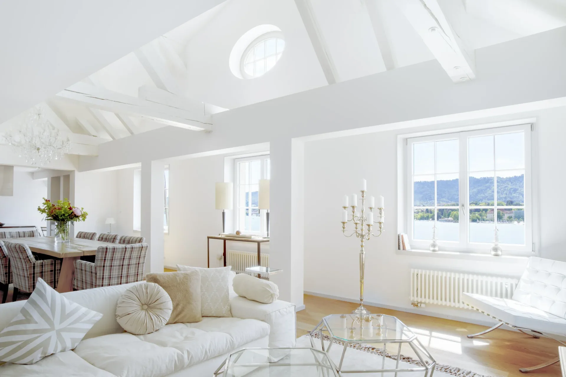 Bright white living room under a beamed roof with sofa, dining table and windows facing Lake Zurich
