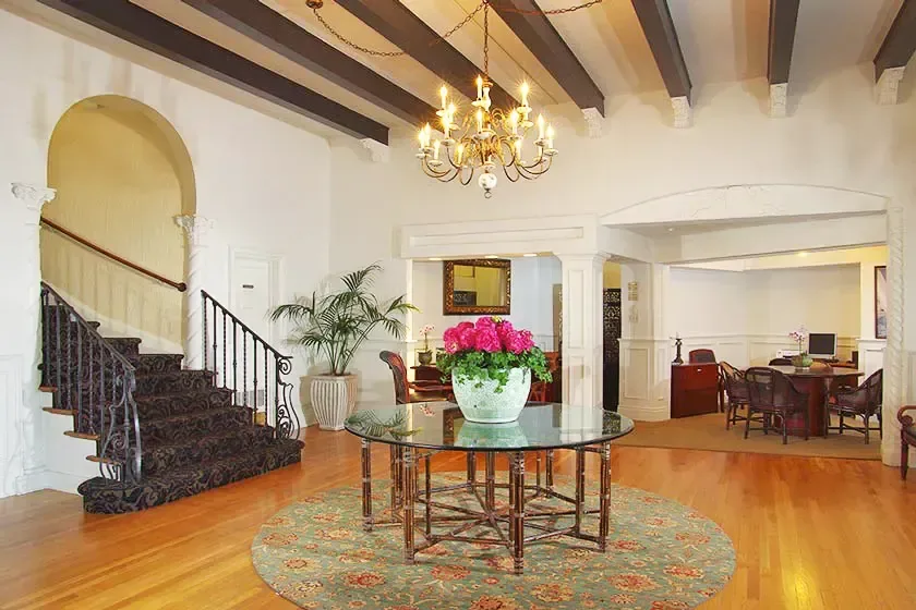 Entrance hall with beamed ceiling, chandelier, round glass table with flowers and a curved staircase