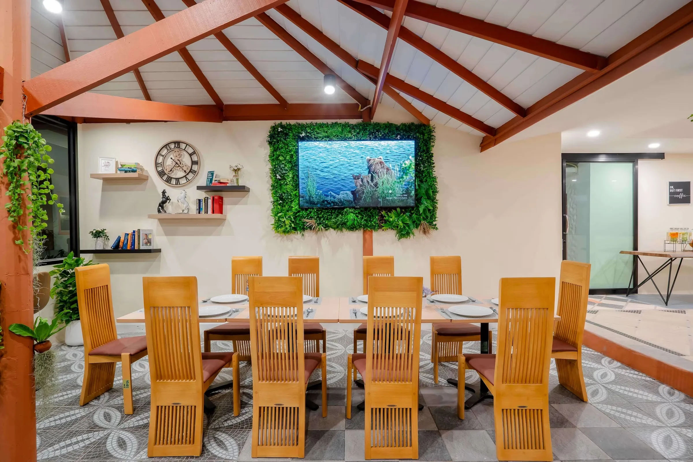 Dining area under an open timber roof with a long table, wooden chairs and a living plant wall