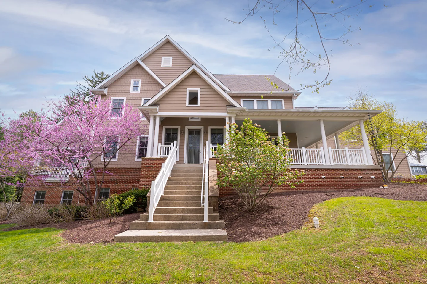 Ruxton House, a gabled family home with a front porch, stone steps and a flowering redbud tree on a lawn