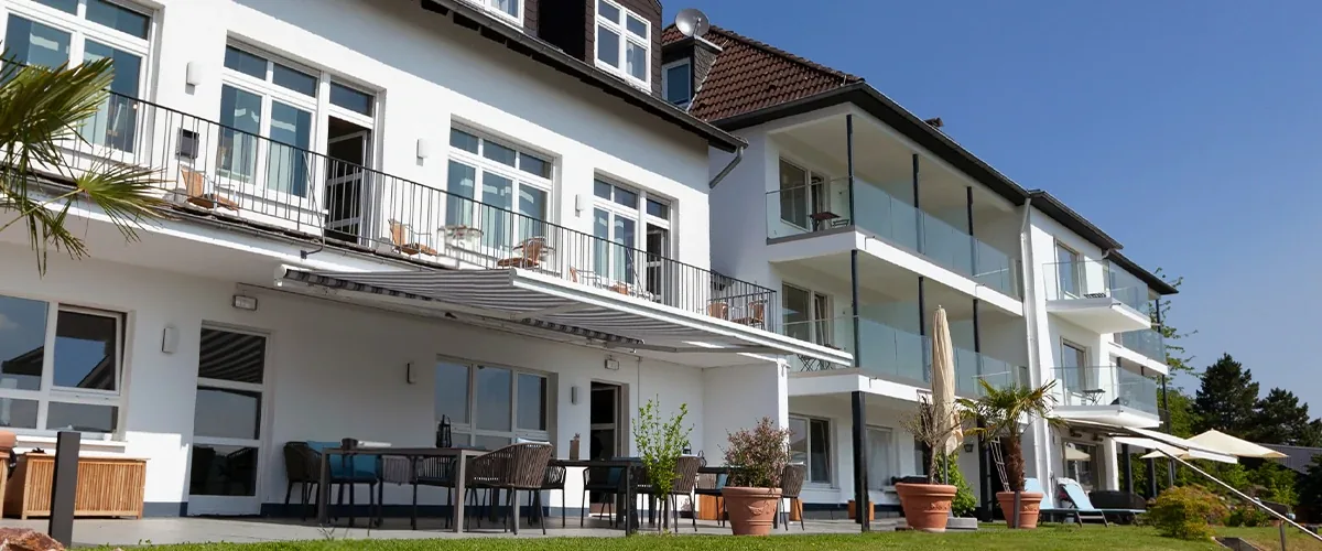 White clinic building with balconies and a terrace with tables and potted plants under a blue sky