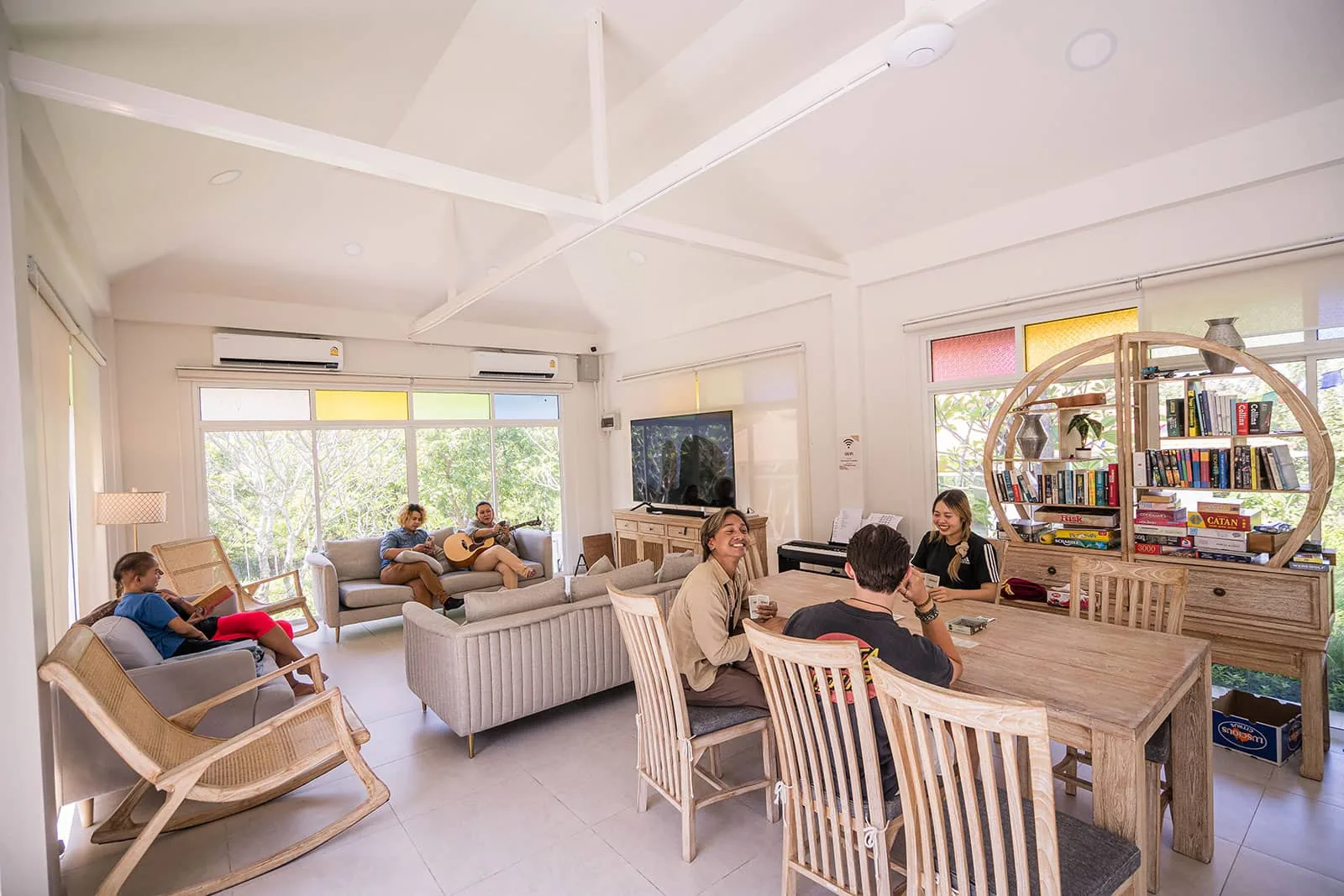 Bright recreation room with a vaulted white ceiling, armchairs, a dining table and bookshelves