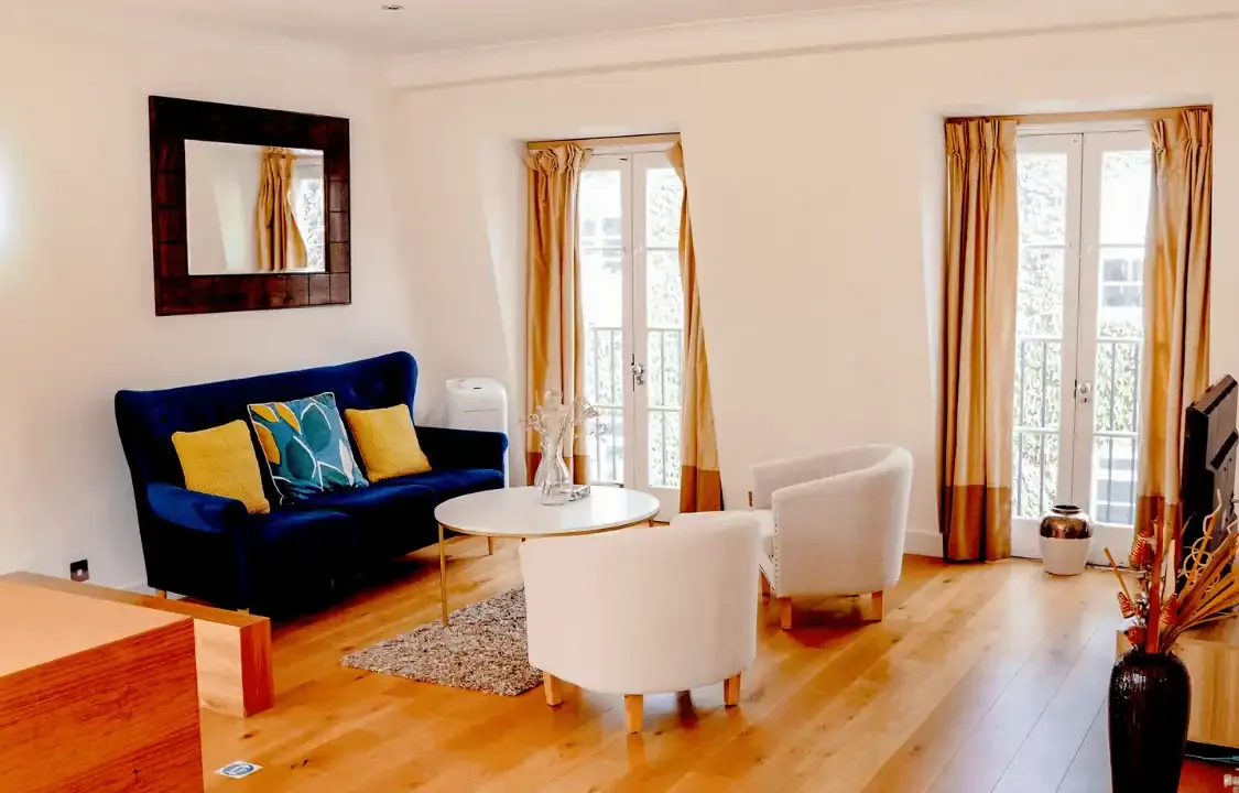 Lounge with a navy sofa, white tub chairs, oak floor and tall French windows with gold curtains