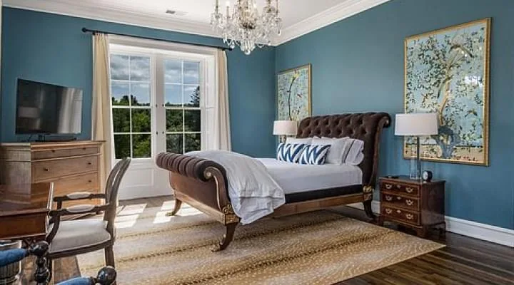Bedroom with blue walls, a dark wooden sleigh bed, crystal chandelier and French doors to a garden