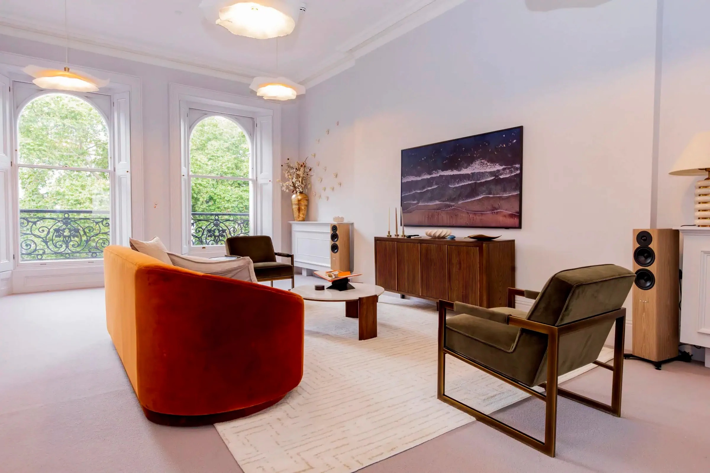 Bright lounge with a curved orange sofa, armchairs and tall arched windows onto green trees
