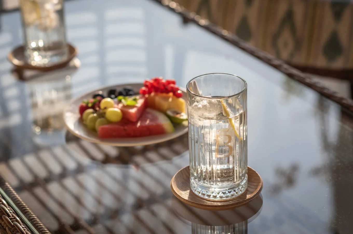 Plate of fresh cut fruit and a glass of water on a glass-topped table in the shade