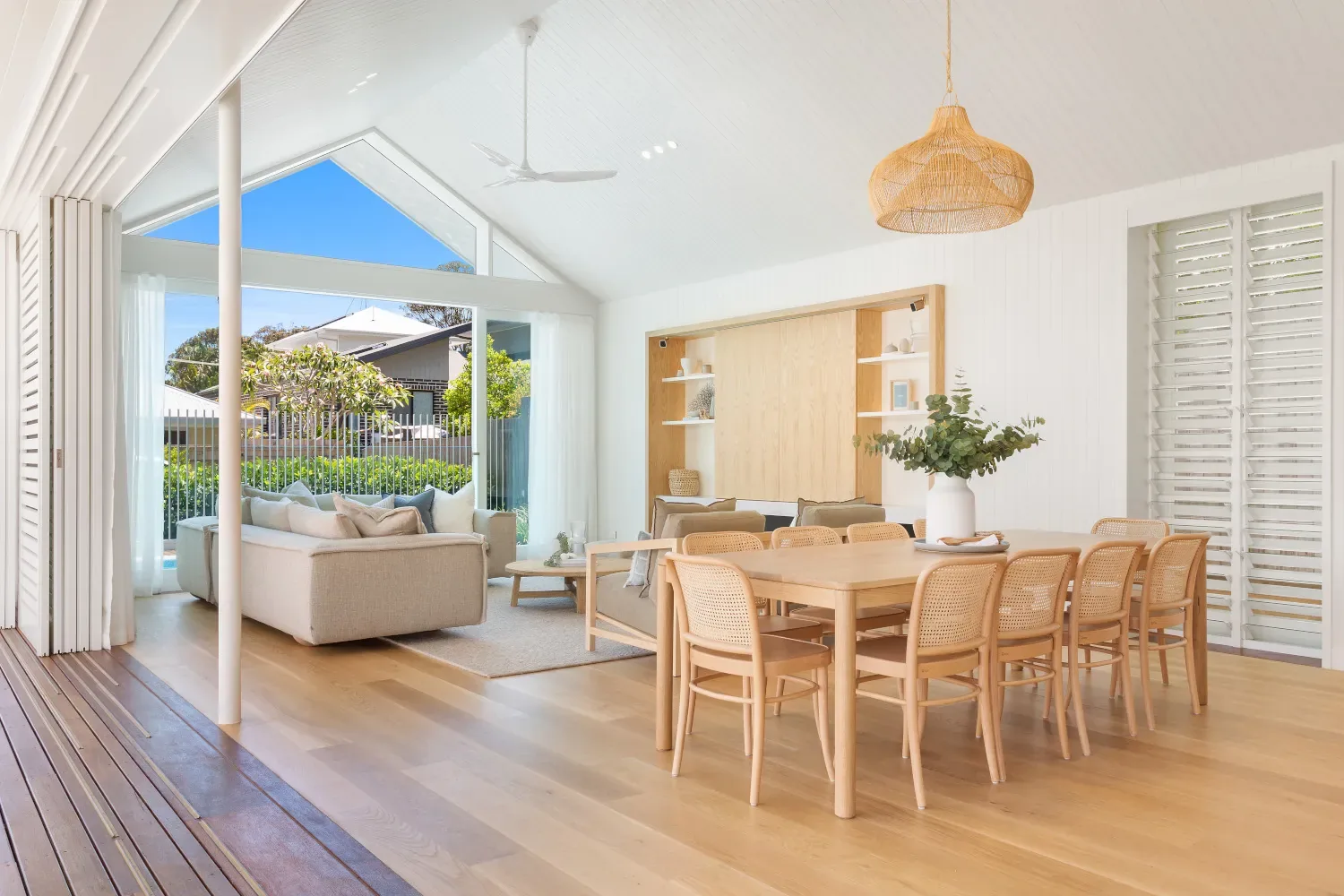 Open lounge and dining room with a cream sofa, timber table and a high gabled ceiling