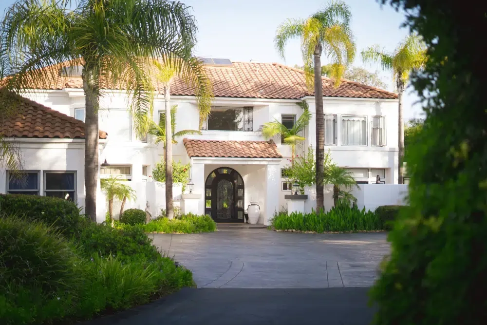 Driveway leading to a white two-storey house with a red tile roof, arched door and palm trees