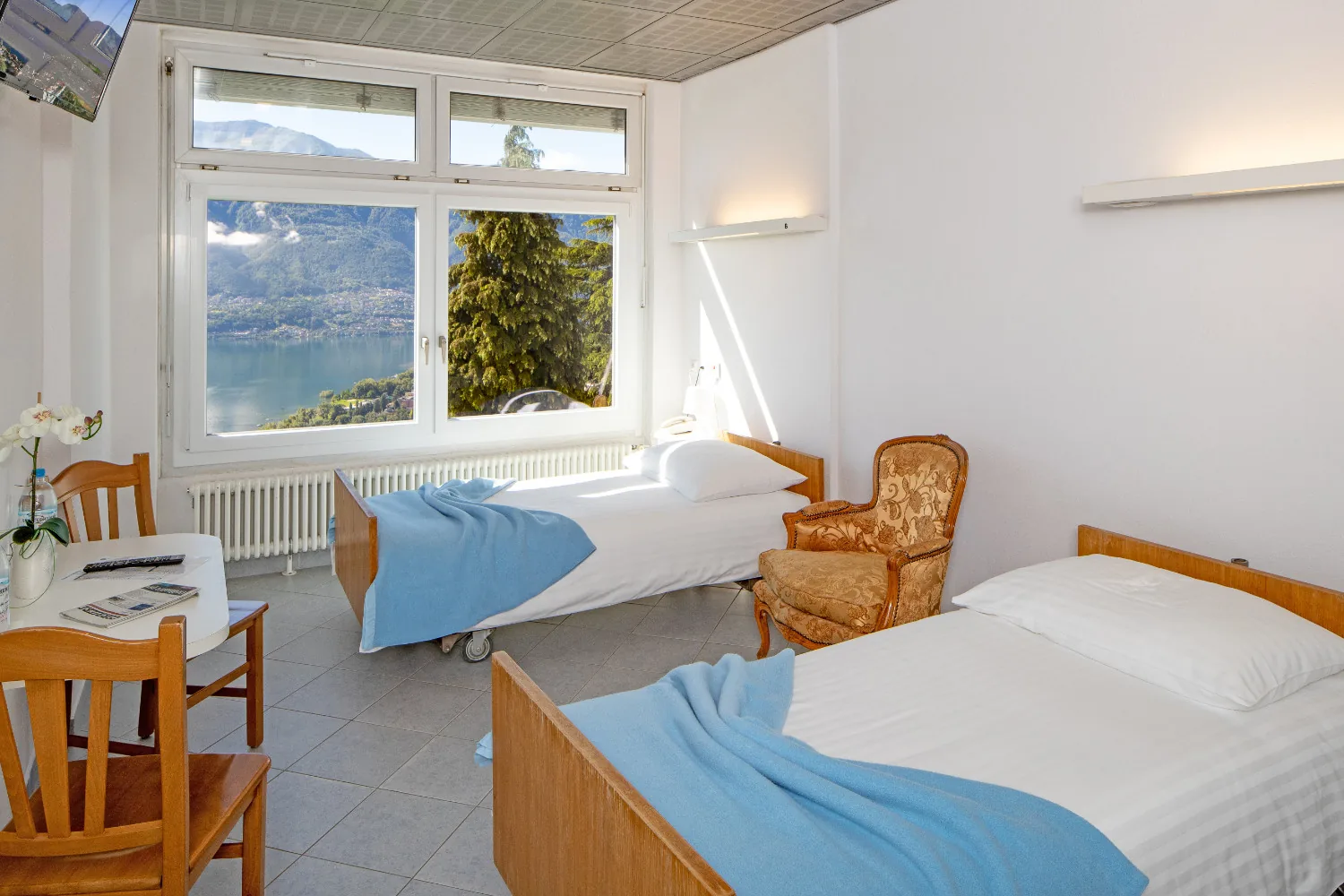 Double room with two wooden beds, blue blankets, armchairs and a window over the lake