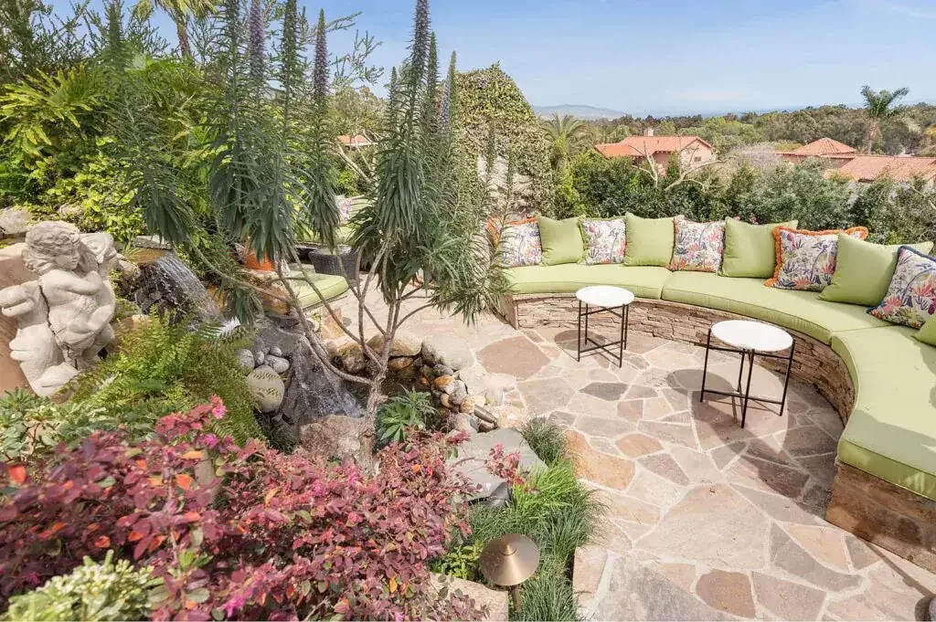 Flagstone patio with a curved cushioned bench, small tables and planted garden beds at Portshead House