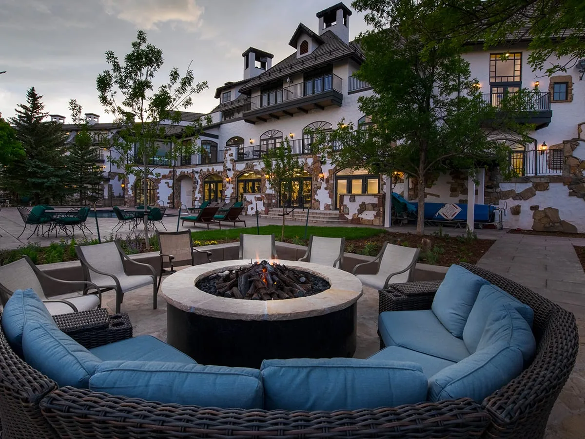 Round outdoor fire pit with curved blue-cushioned seating in front of the lodge facade