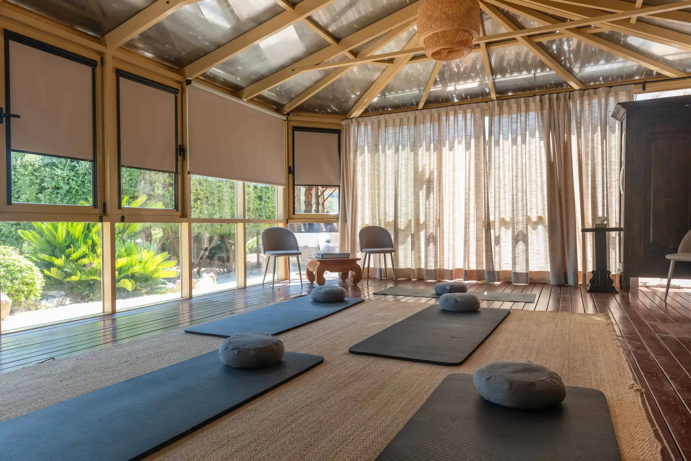 Yoga studio under a timber roof with mats and cushions laid out and windows onto the garden