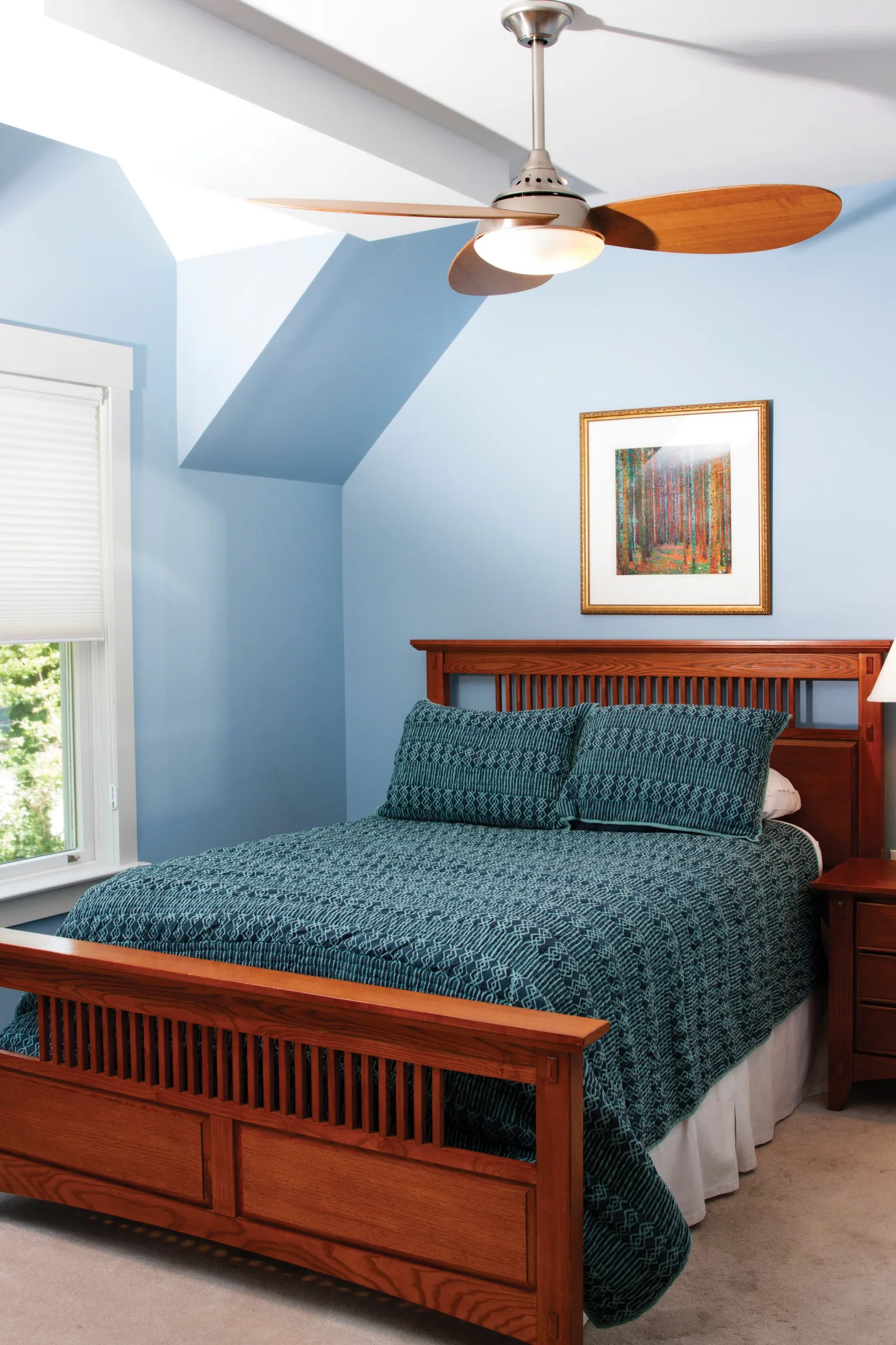 Bedroom under a sloped blue ceiling with a wooden bed, patterned quilt and a ceiling fan